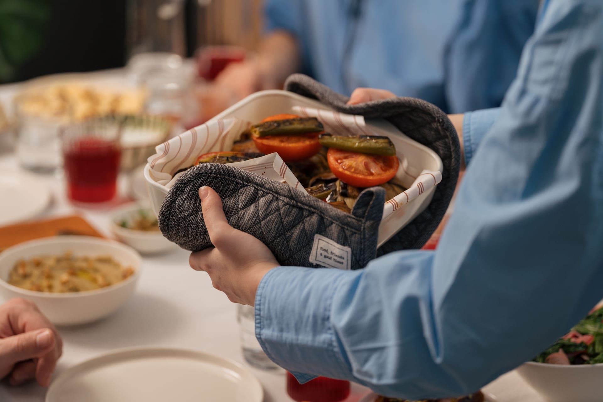 Hands carrying a baking dish of roasted vegetables to a table